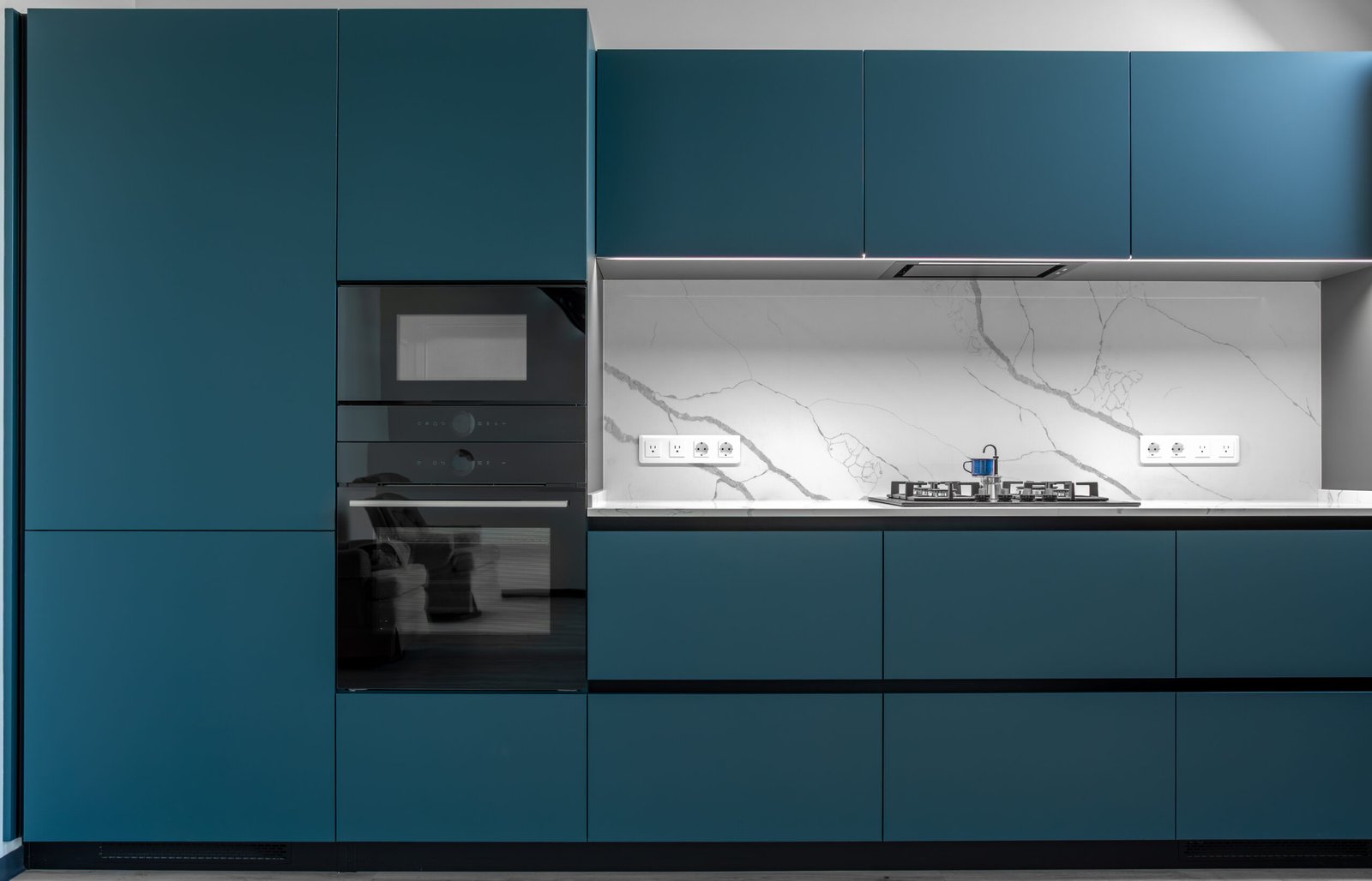 Contemporary kitchen with built-in oven, marble backsplash, and sleek matte blue cabinetry. Functional, stylish and compact cooking zone.